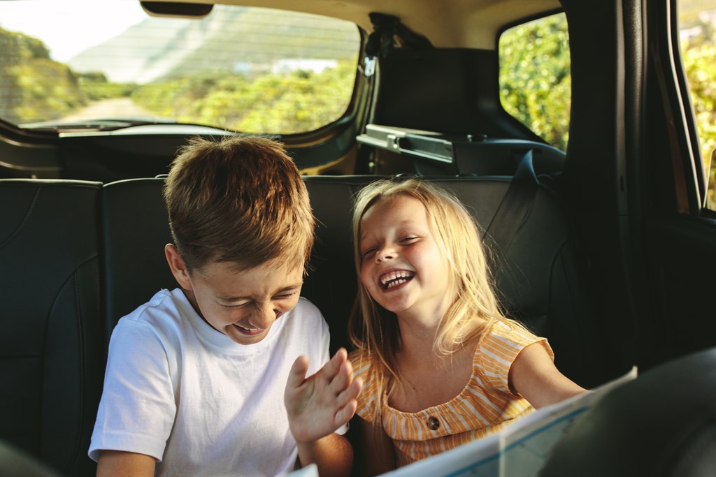 Young brother and sister laughing in the backseat during a road trip.