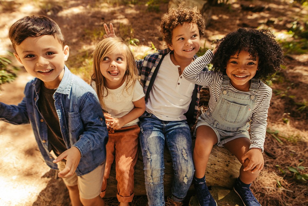 Group of four kids sitting on a wooden log and having fun.