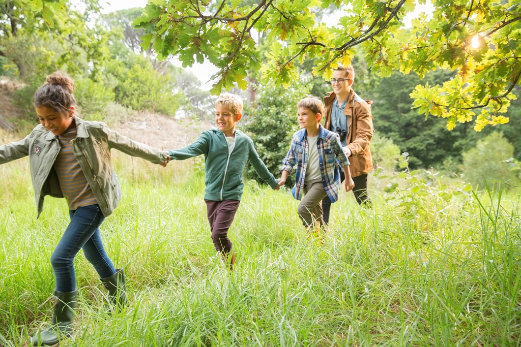 Three kids and adult hold hands while on a nature trail.