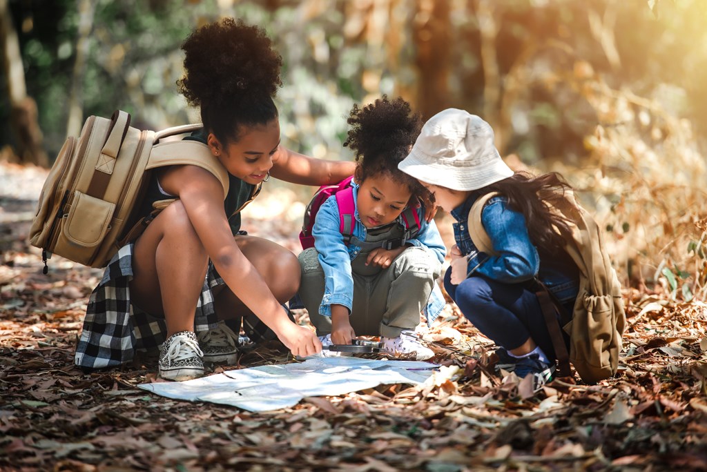 Three young girls look at a map on the forest floor as part of a scavenger hunt.