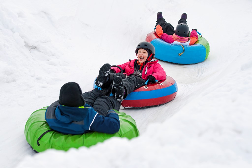 Three kids laughing as they slide down a snowy hill in innertubes.