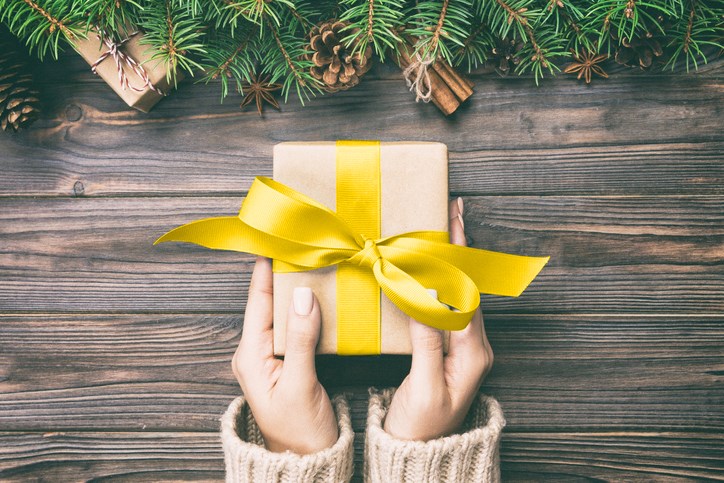 A person holding a small brown box with a yellow ribbon around it.