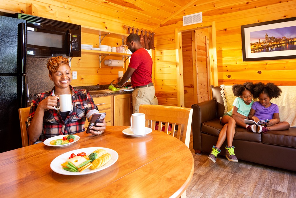 A family of four enjoys the living room and kitchenette in a KOA Deluxe Cabin.