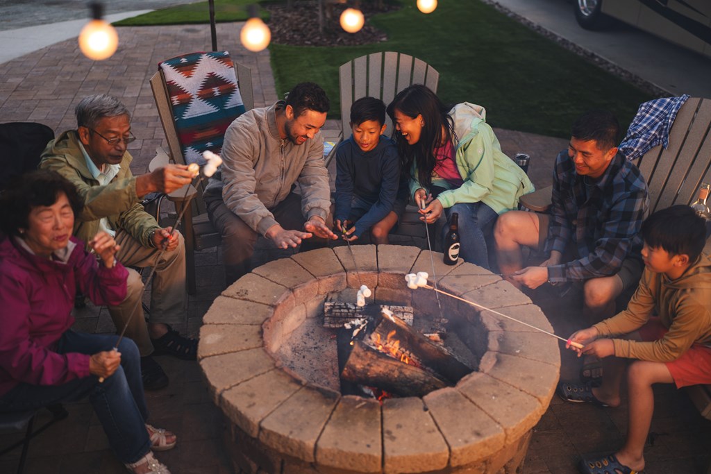 A group of multi-generational family gather around a campfire at a KOA RV site.