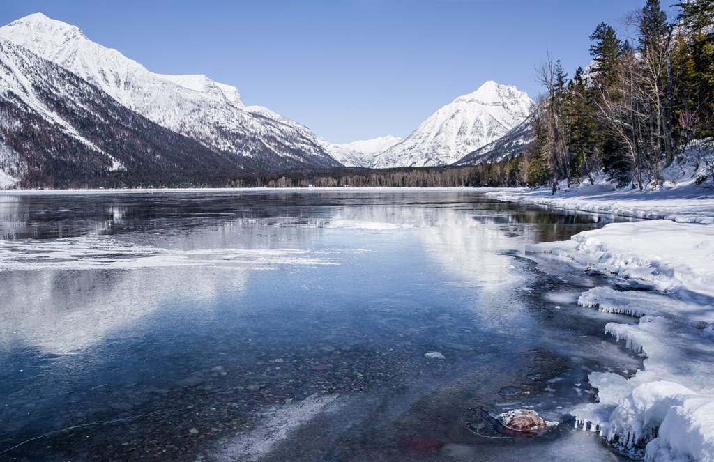 Snow covered mountains reflect from the icy surface of Lake McDonald in Glacier National Park.