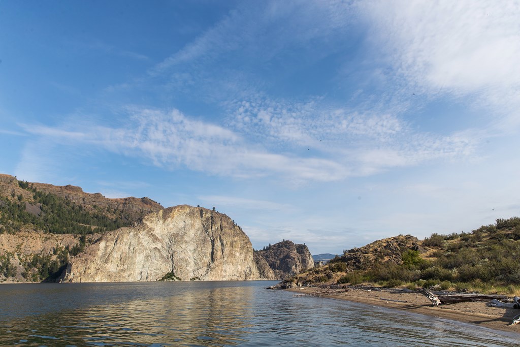 A view of Lake Roosevelt in Washington State with steep cliffs to the left and calm shore to the right.