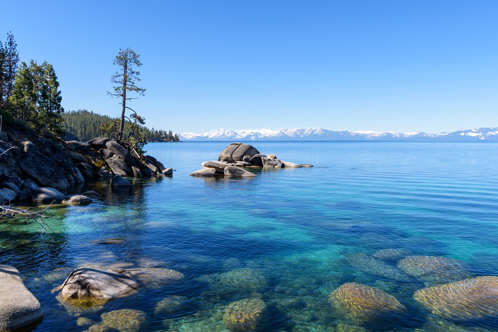 Landscape of blue Lake Tahoe with snowcapped mountains and clear blue sky behind, California
