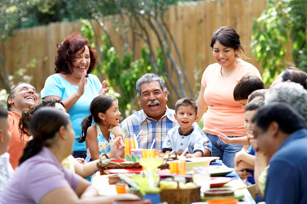 A multi-generational family gathers around a large table to dine outdoors.