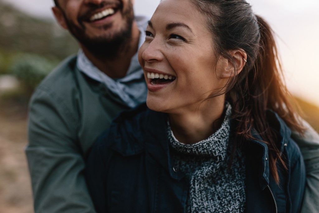 A woman smiles as her partner embraces her on a hike.