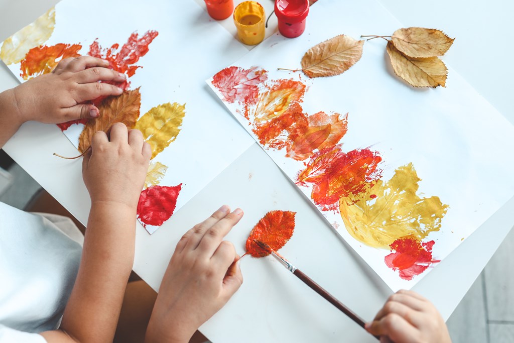 Children painting fall leaves an imprinting them on paper.