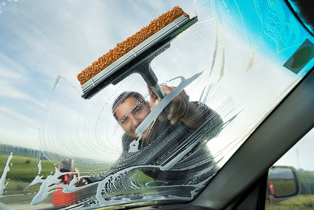 Man using a squeegee to clean the windshield of his car. 