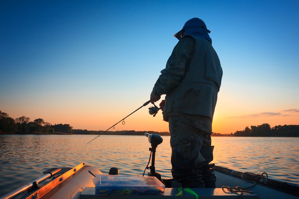 A fisherman fishing in a lake at sunset on a boat.