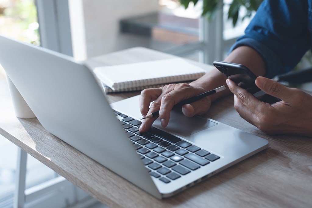 Closeup of a man using a phone and laptop.