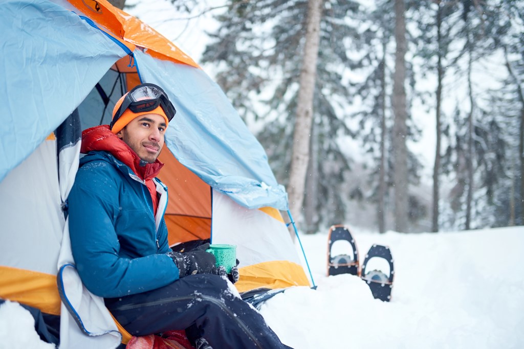 Man sitting at the door of his tent looking out over the winter snow.