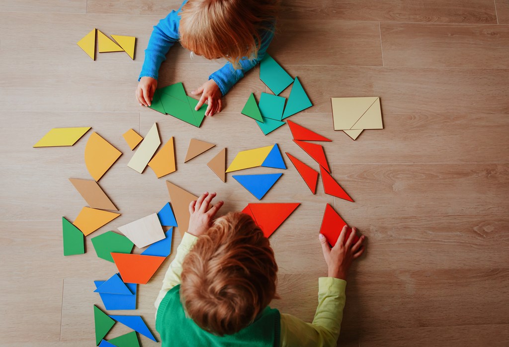 A little boy and little girl play with a math puzzle game on the floor.