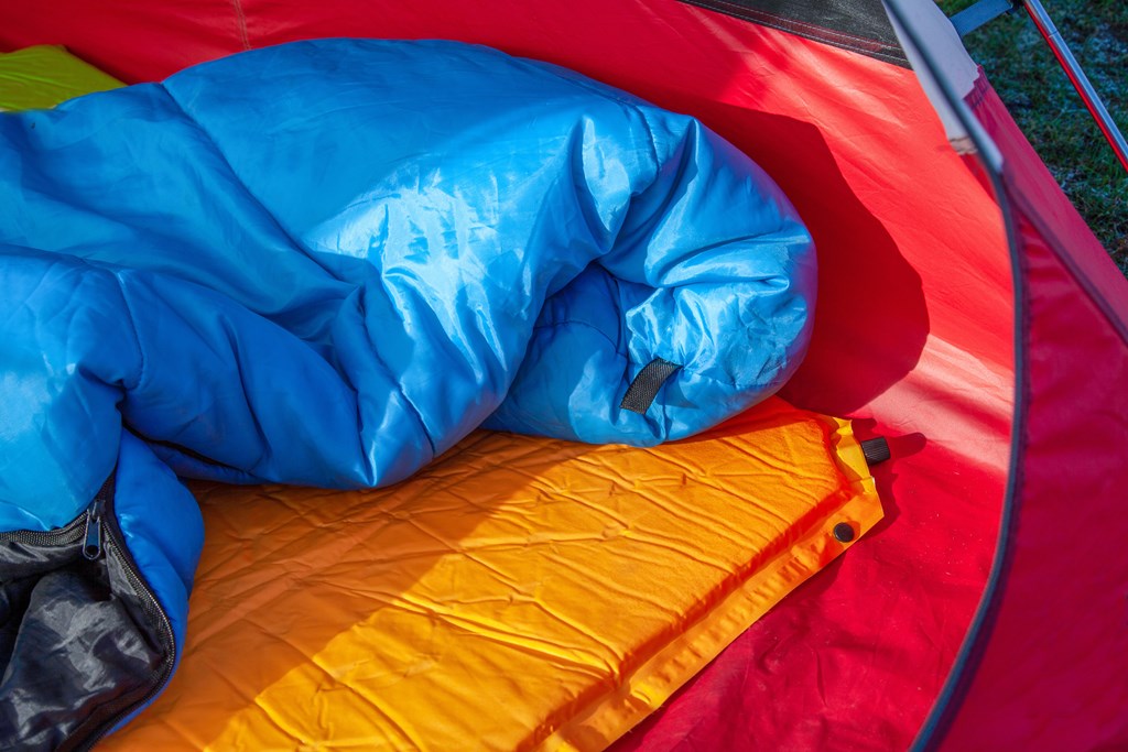 The inside of a red tent with an blue sleeping bag and an orange self-inflating blow-up mattress pad for under his sleeping bag.