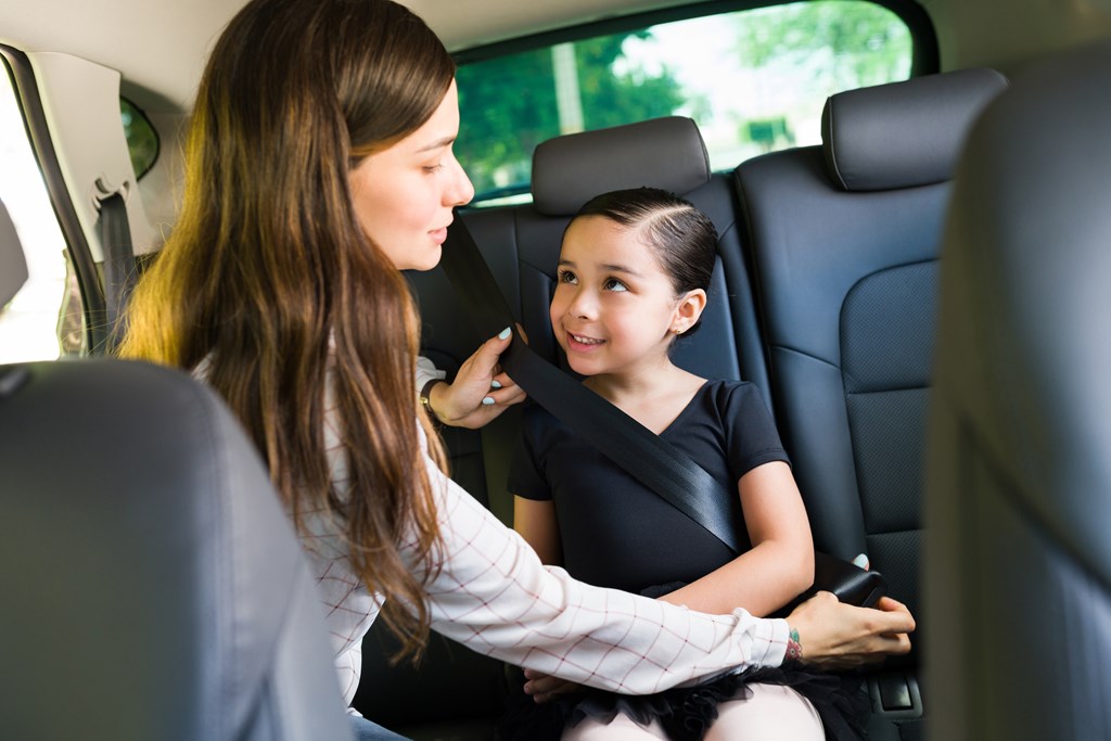 Mom buckles her young daughter into the backseat of an SUV.