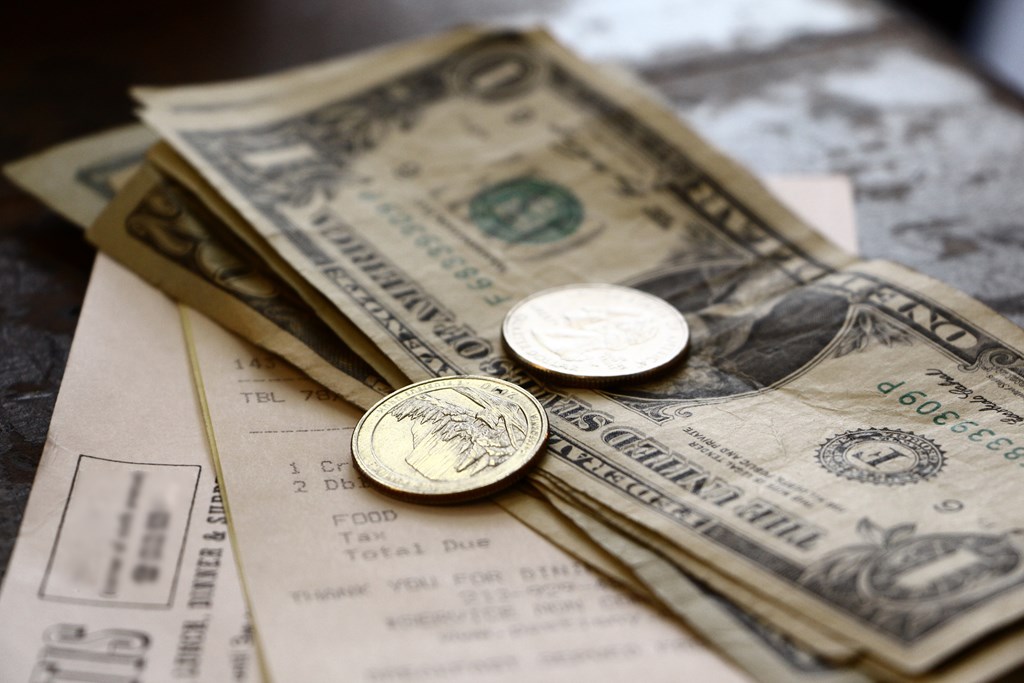 Dollar bills and a few coins sit on top of a restaurant receipt. 