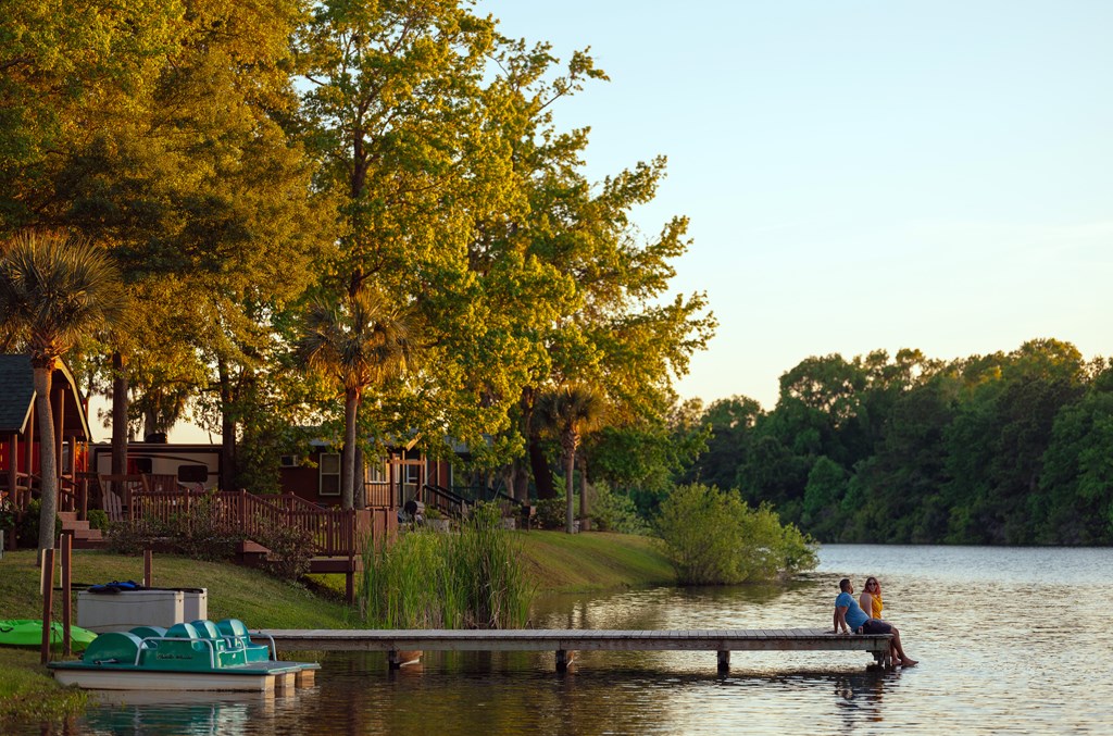 A couple sits on the end of a lakeside dock at a KOA campground.