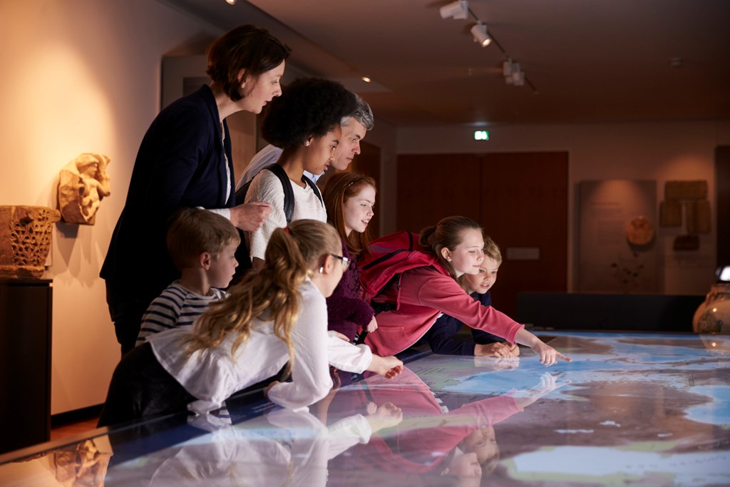 Students on a field trip look at a digital display in a history museum.