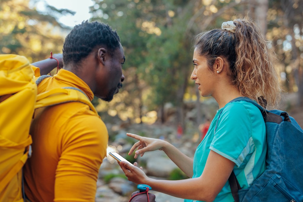 Two hikers are checking an online map on a smartphone to navigate their way through the mountains.