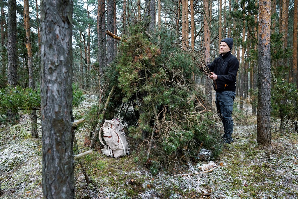 Man building a shelter with pine branches in the forest.