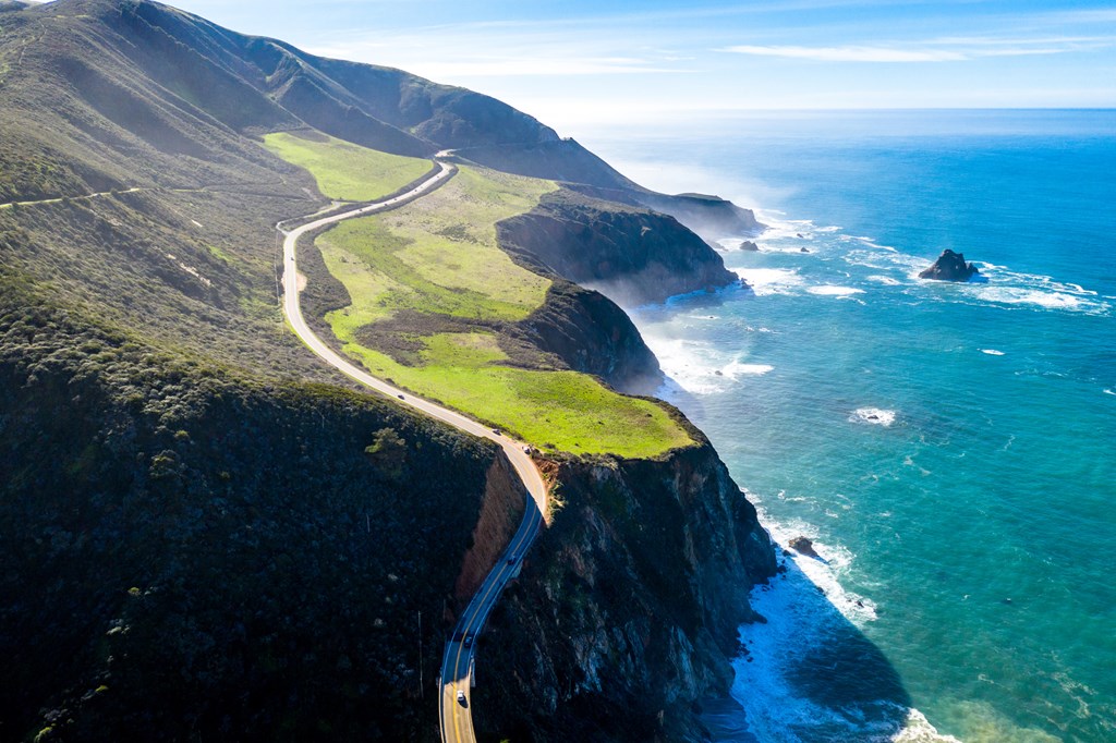 Aerial view of California's Highway 1 as it winds along the green hills of the Pacific coast.