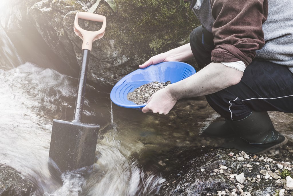 Gold panning, man is looking for gold with a gold pan in a small stream. 