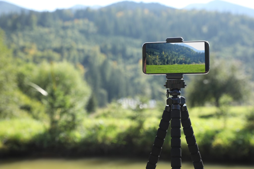 Taking photo of beautiful mountain landscape with smartphone mounted on tripod outdoors.