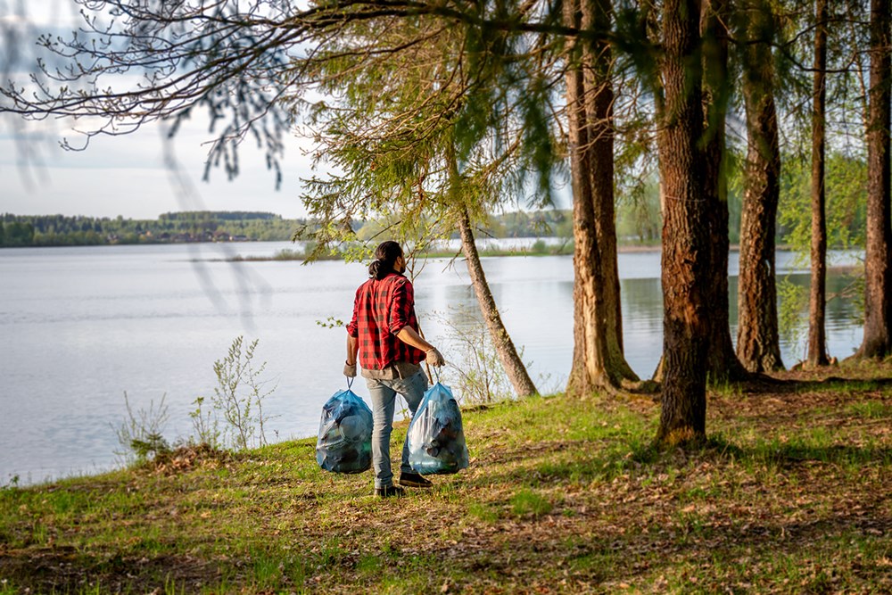 Young man with bags of trash cleaning the green forest from household rubbish, environmental problems recycling of plastic.