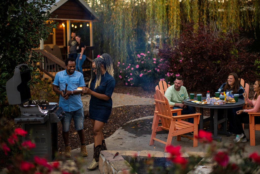 A group of friends enjoy dinner from the grill on the patio of a KOA Deluxe Cabin.