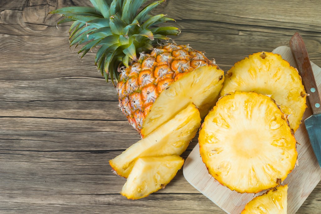 A cut pineapple on a wooden background.