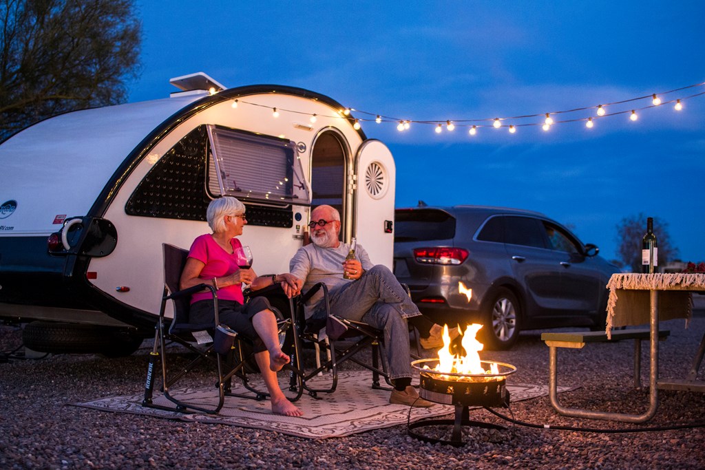 An older couple enjoys an evening by the fire in front of their small towable RV.
