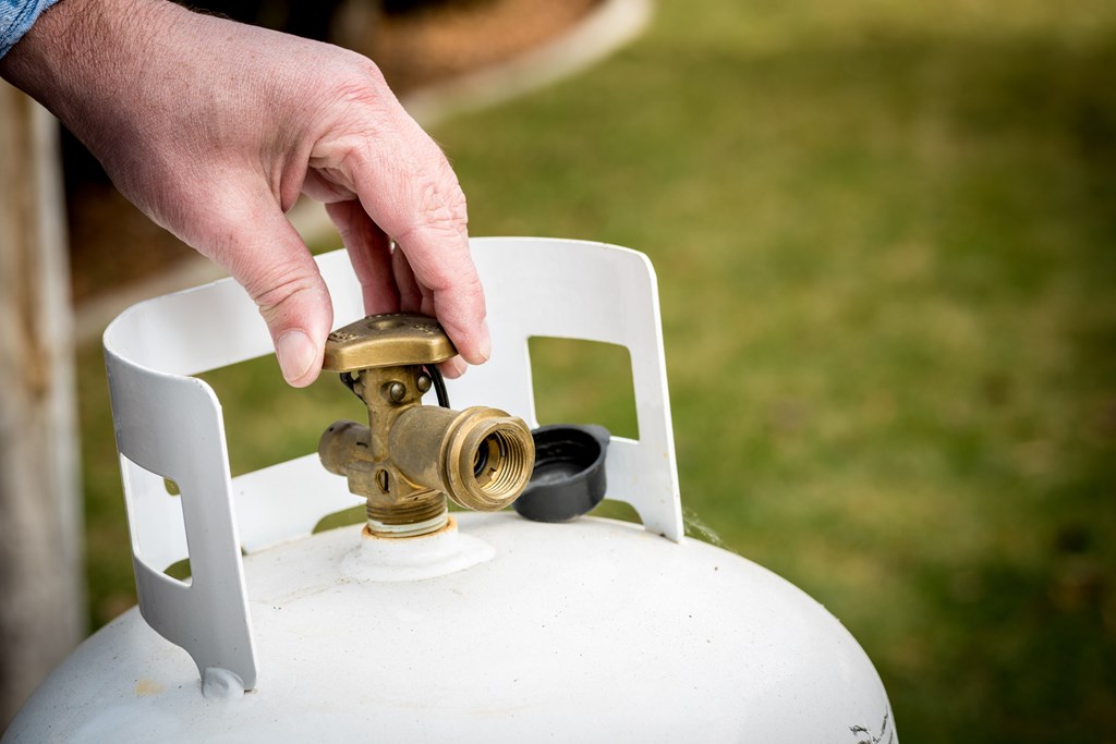 Close-up of a man adjusting the valve on a propane-tank.