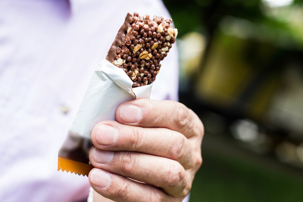 Close up of a man holding an open protein bar.