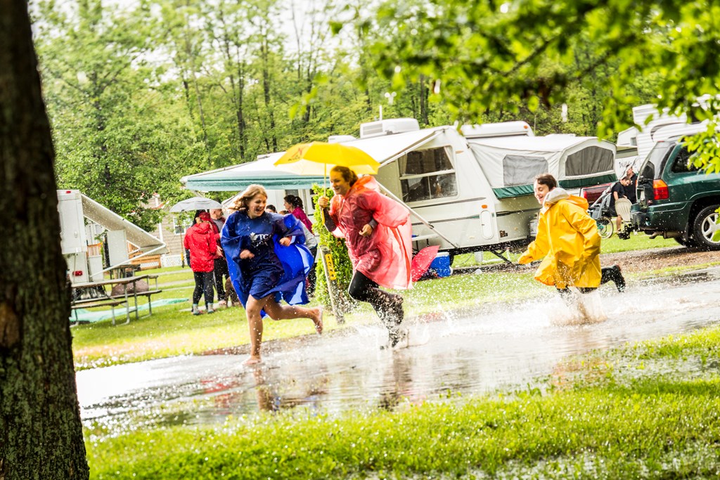 Three kids splash in puddles during a rainstorm at a KOA campground.