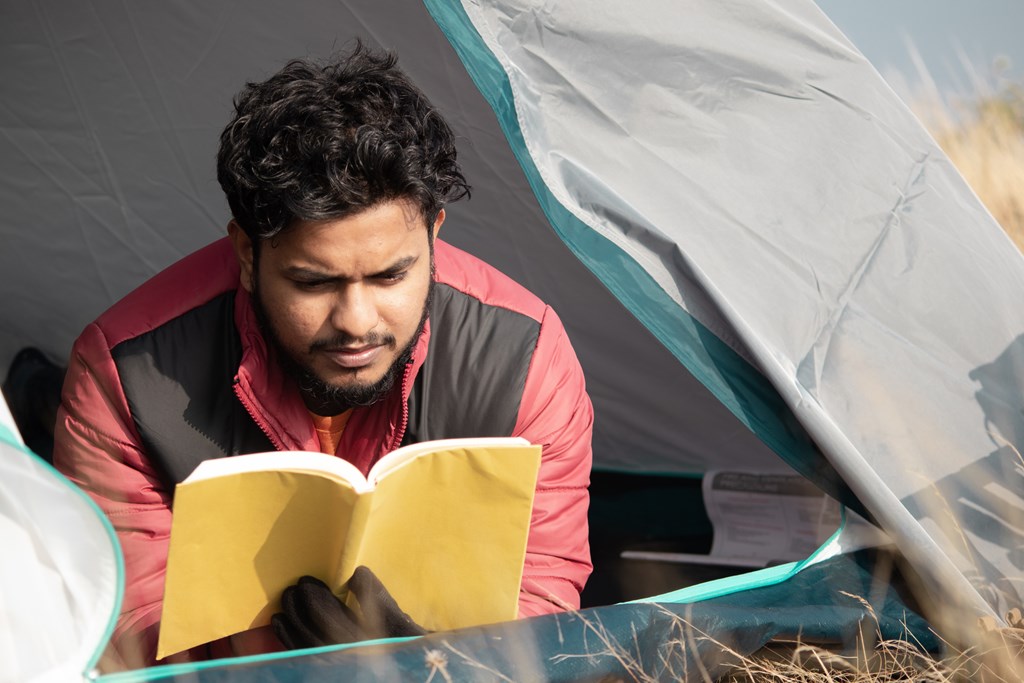 Young traveler reading book inside a tent.