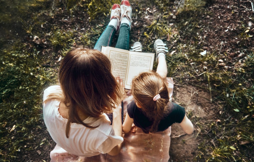 Mom and daughter on a sunny summer day in the park read a book.