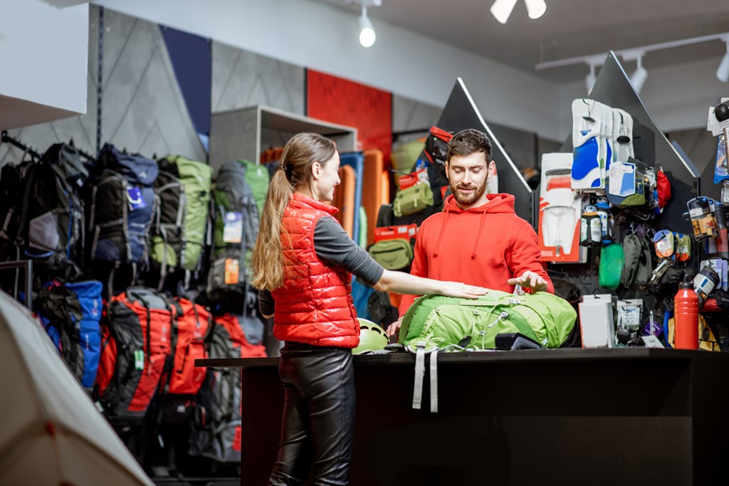 Young woman buying some sports goods standing with salesman at the counter of the shop