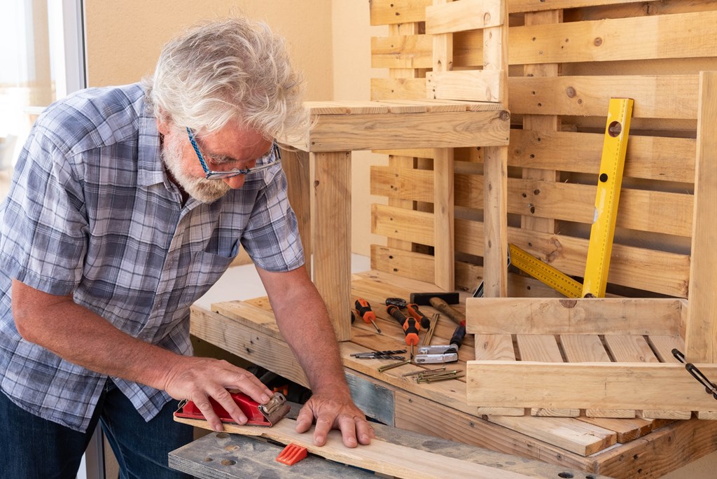 Man with white hair enjoying work with wooden pallet to create new objects for home. 