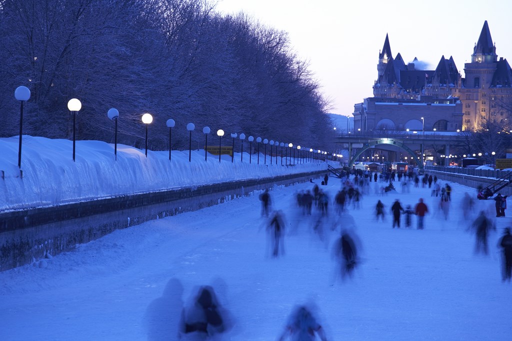 Blurred skaters move quickly along an icy canal at dusk.