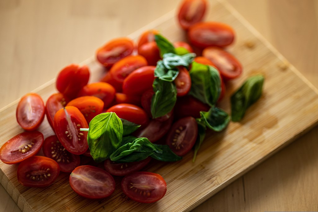 Sliced cherry tomatoes and basil leaves on a wooden background.
