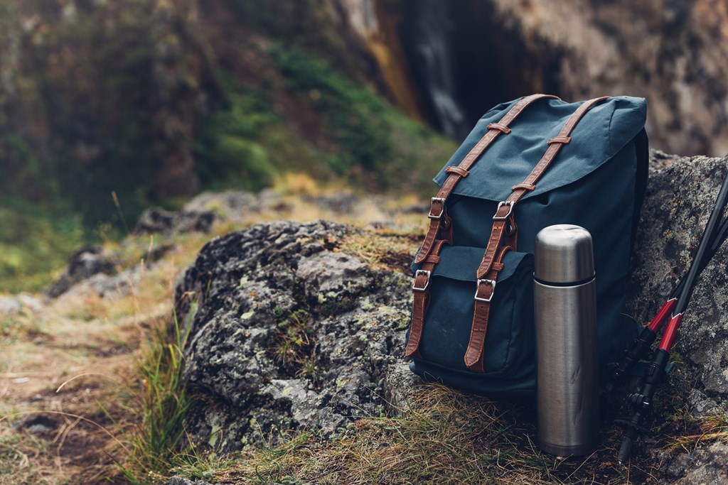 Close-up of a blue hiking backpack, thermos and trekking sticks.