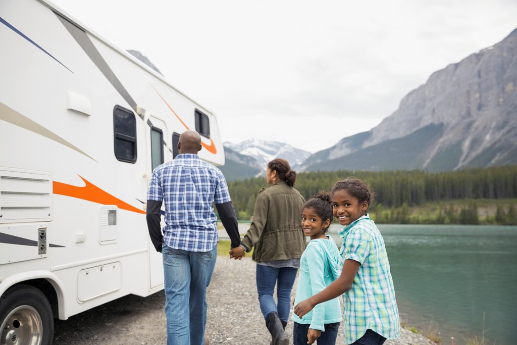 A family of four walks towards their RV parked on a lake.