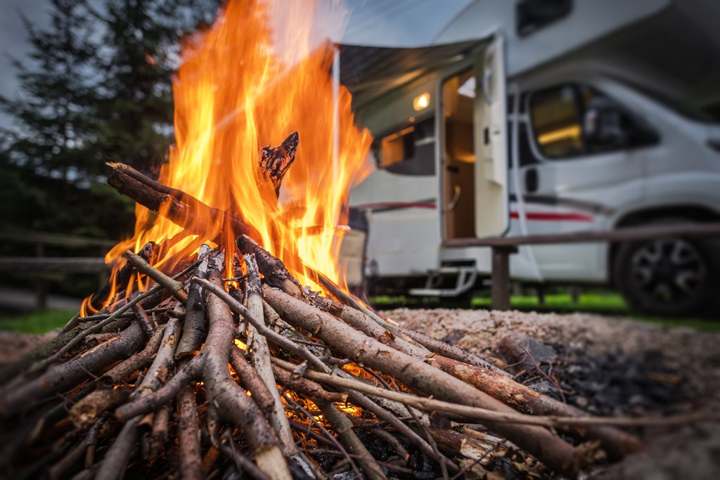 A close up of a campfire with an RV in the background.