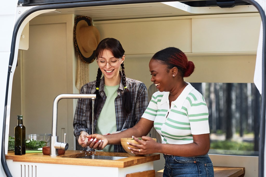 Two women at work in the small kitchen of a camper van.