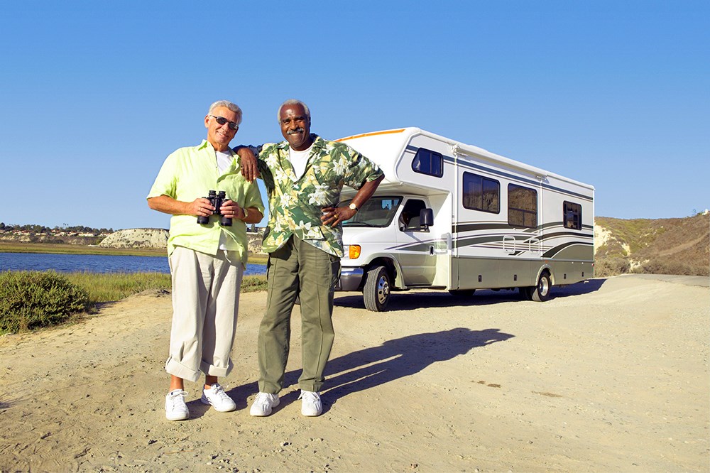 Two men stand in front of an RV smiling