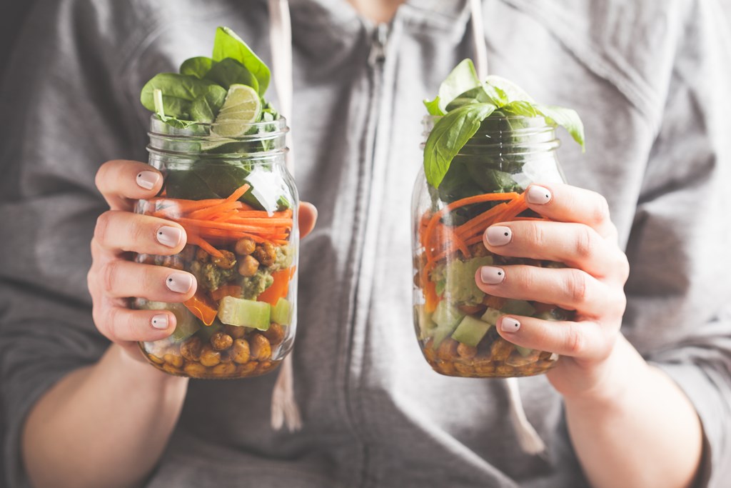 A woman holds two salads in glass jars with baked chickpeas, guacamole and vegetables.