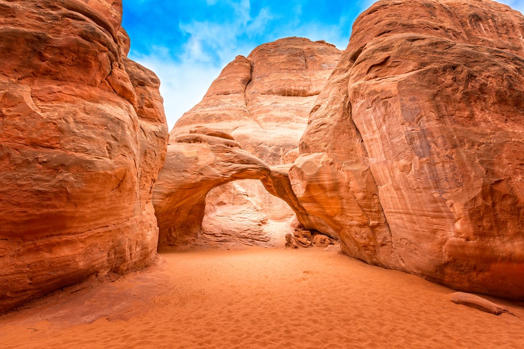 The famous Sand Dune Arch in the Arches National Park, Utah. A red rock arch under a blue sky with wispy clouds.