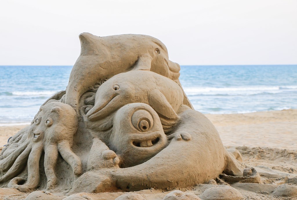 A sand sculpture made of sea creatures including octopus and dolphins on a beach.